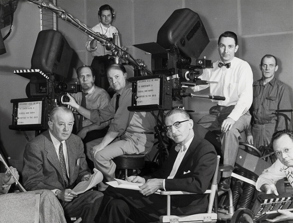 black and white photo of a group of men sitting around cameras with old paper wound autocues
