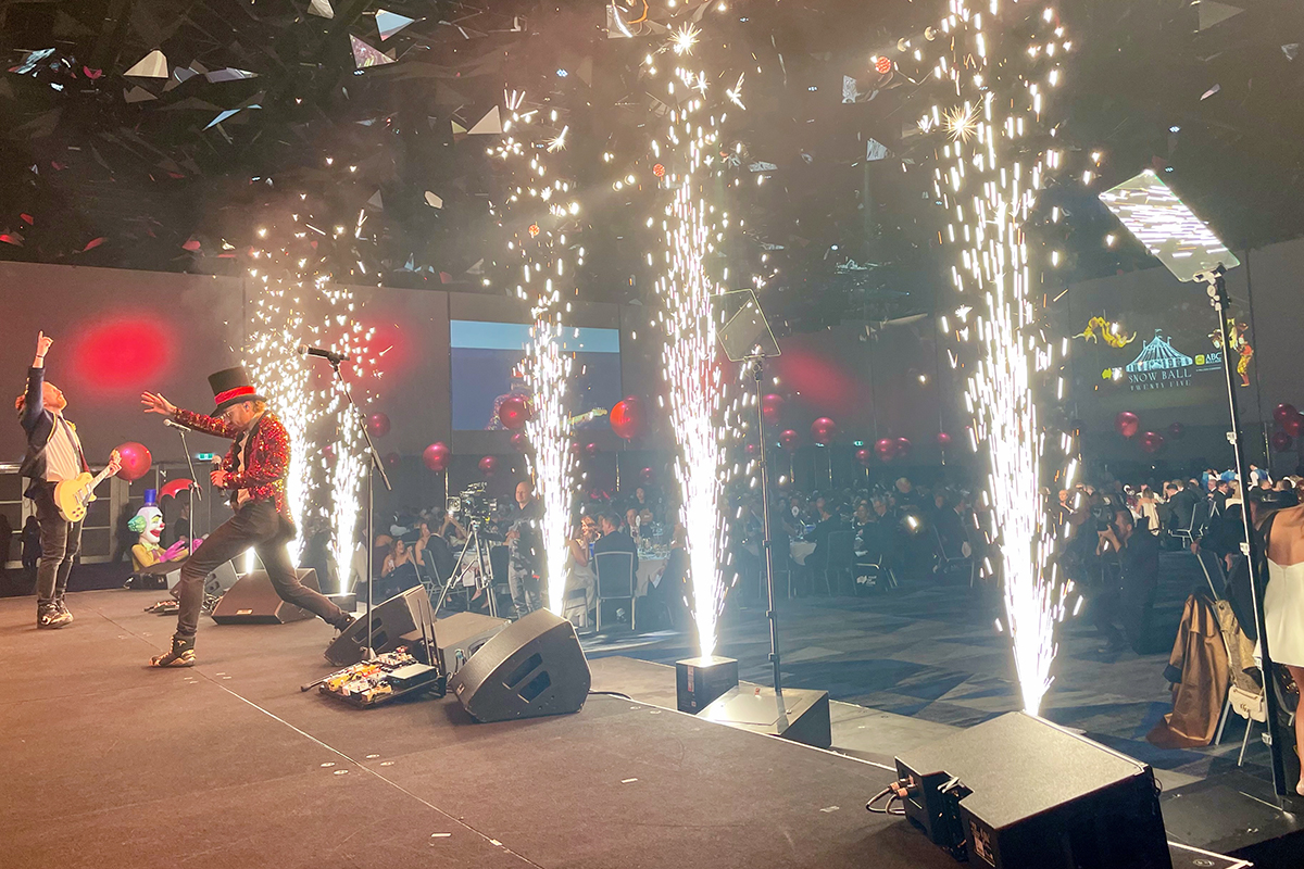 Fireworks going off along the front of a stage, next to the Teleprompters